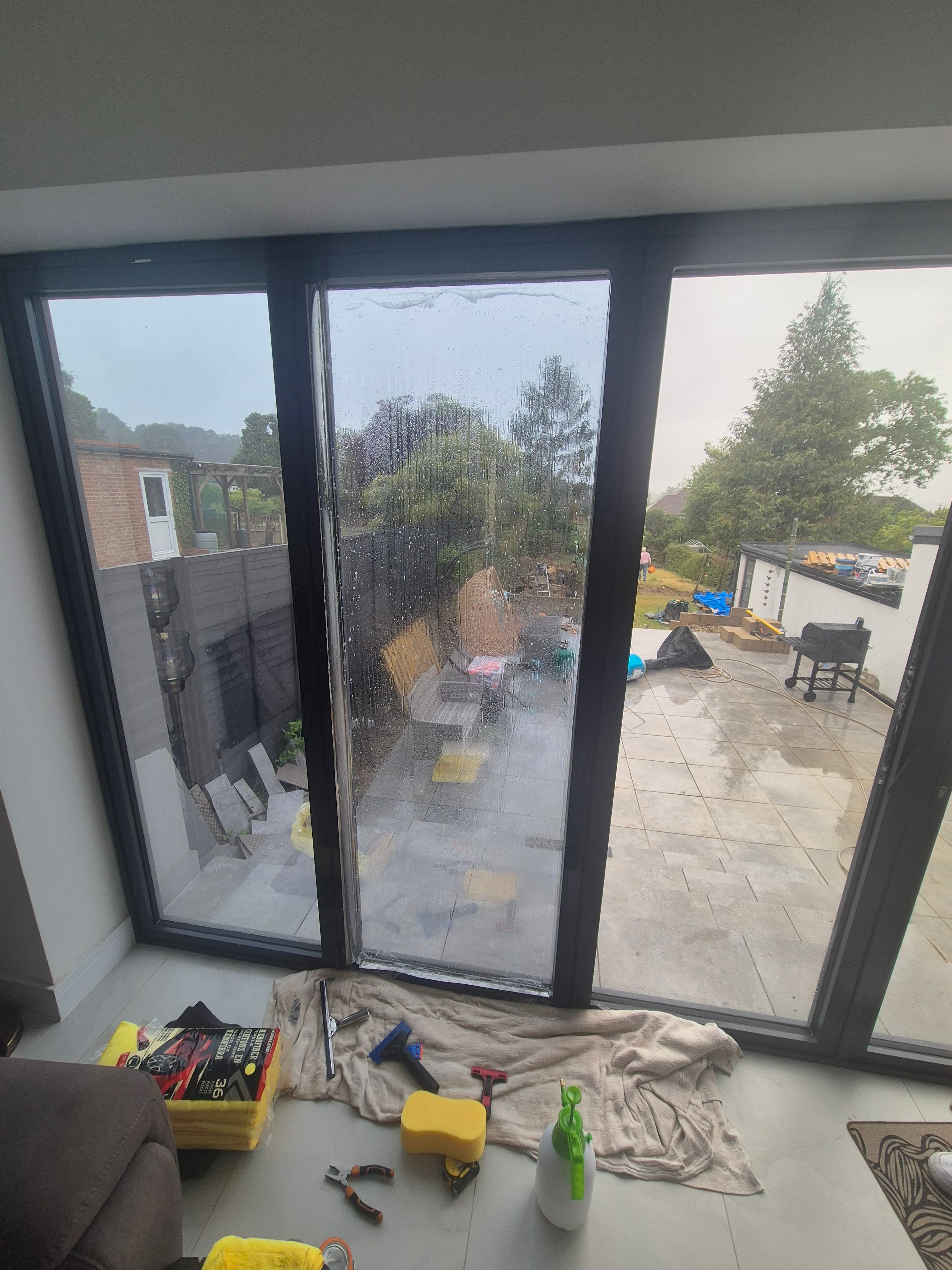 Window film being applied to a bifold door in an Uxbridge property, with tools and a dust sheet visible as the installer smooths the film onto the glass.